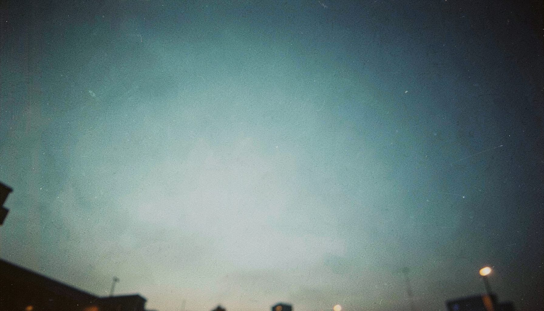 Soft gradient sky of muted teal and deep navy blue with hazy evening light and gentle film grain, creating a calm dusk atmosphere